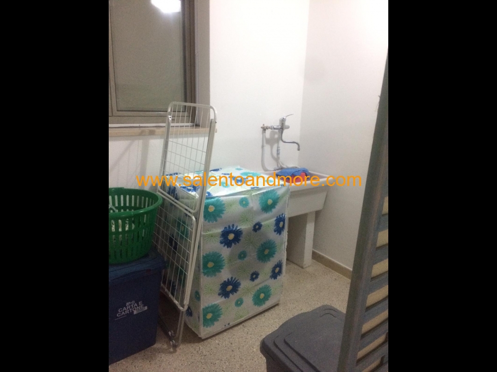 Zona lavanderia con lavatrice, lavabo e stendibiancheria. 