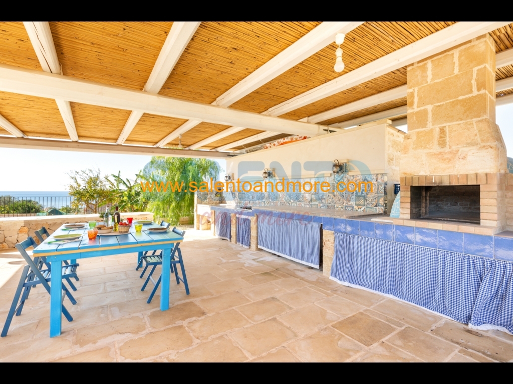 Tavolo. sedie, forno a legna, barbecue, cucina e lavabo.